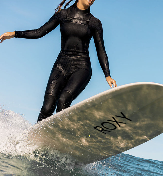 A woman in a black steamer wetsuit riding a surfboard on a wave